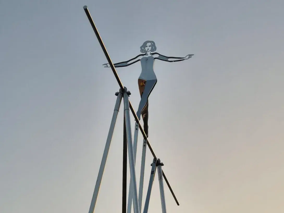 Tightrope walker sculpture silhouetted against a sunset